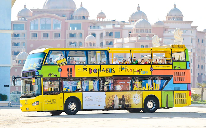 Doha hop-on hop-off tour bus in front of traditional architecture.