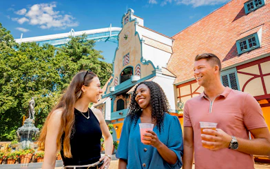 Visitors enjoying drinks at Busch Gardens Williamsburg with a themed building in the background.