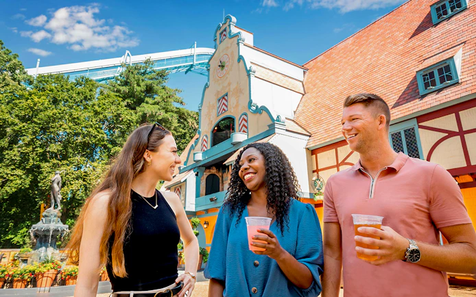 Visitors enjoying drinks at Busch Gardens Williamsburg with a themed building in the background.