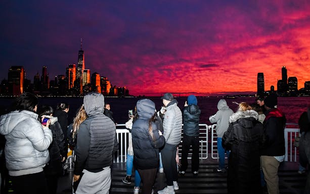 Guests on Statue of Liberty sightseeing cruise at sunset with New York City skyline.