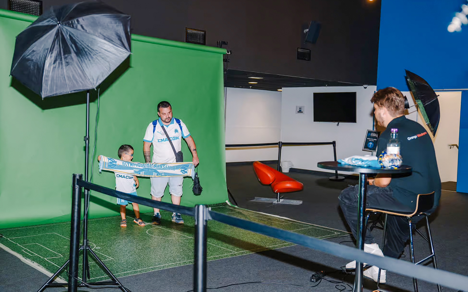 Father and child posing with a Marseille scarf at Velodrome stadium tour photo area.