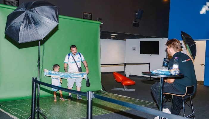 Father and child posing with a Marseille scarf at Velodrome stadium tour photo area.