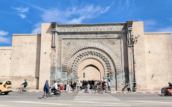 Ornate entrance of Ben Youssef Medersa with people and cyclists, Marrakech.