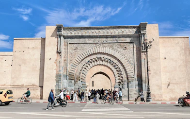Ornate entrance of Ben Youssef Medersa with people and cyclists, Marrakech.