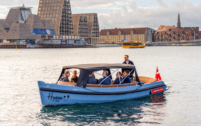 Copenhagen canal tour boat with passengers near modern architecture.