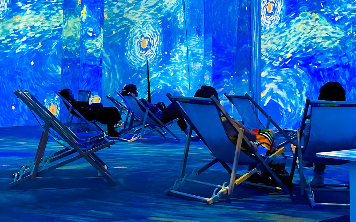 Guests relaxing in deck chairs at Van Gogh Exhibition, London, surrounded by immersive art projections.