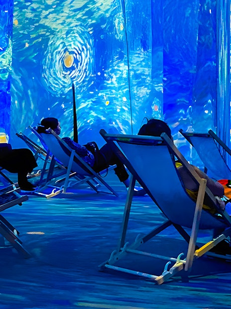 Guests relaxing in deck chairs at Van Gogh Exhibition, London, surrounded by immersive art projections.