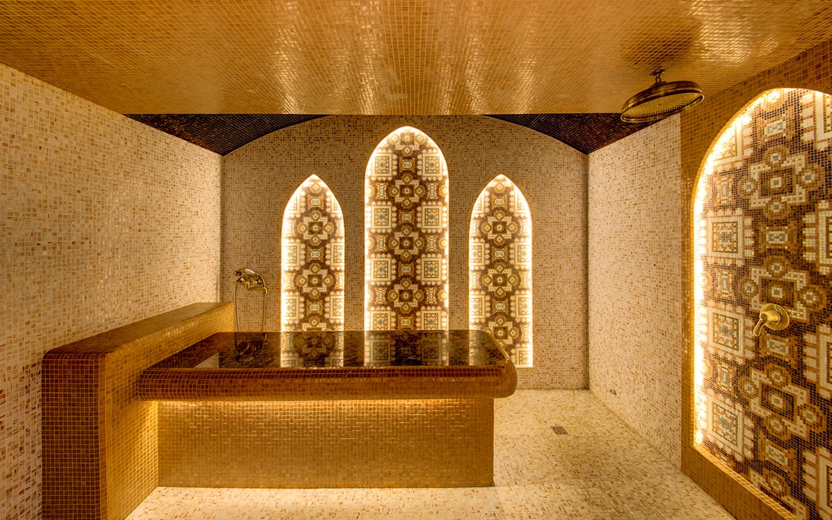 Interior of Sifa Hamam with ornate mosaic walls and central stone table.