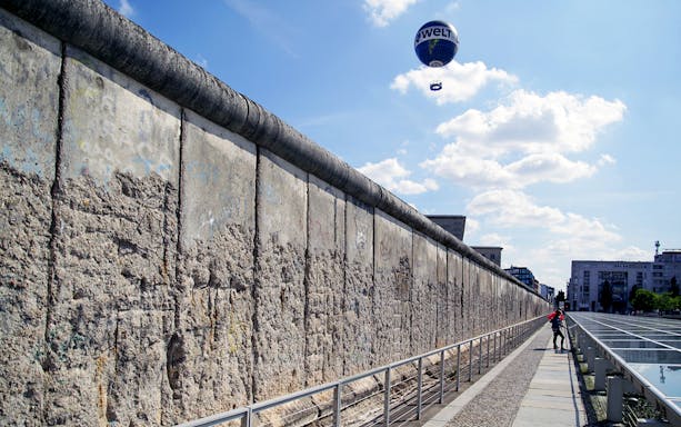 Berlin Wall with a hot air balloon in the sky and a person walking along the path.