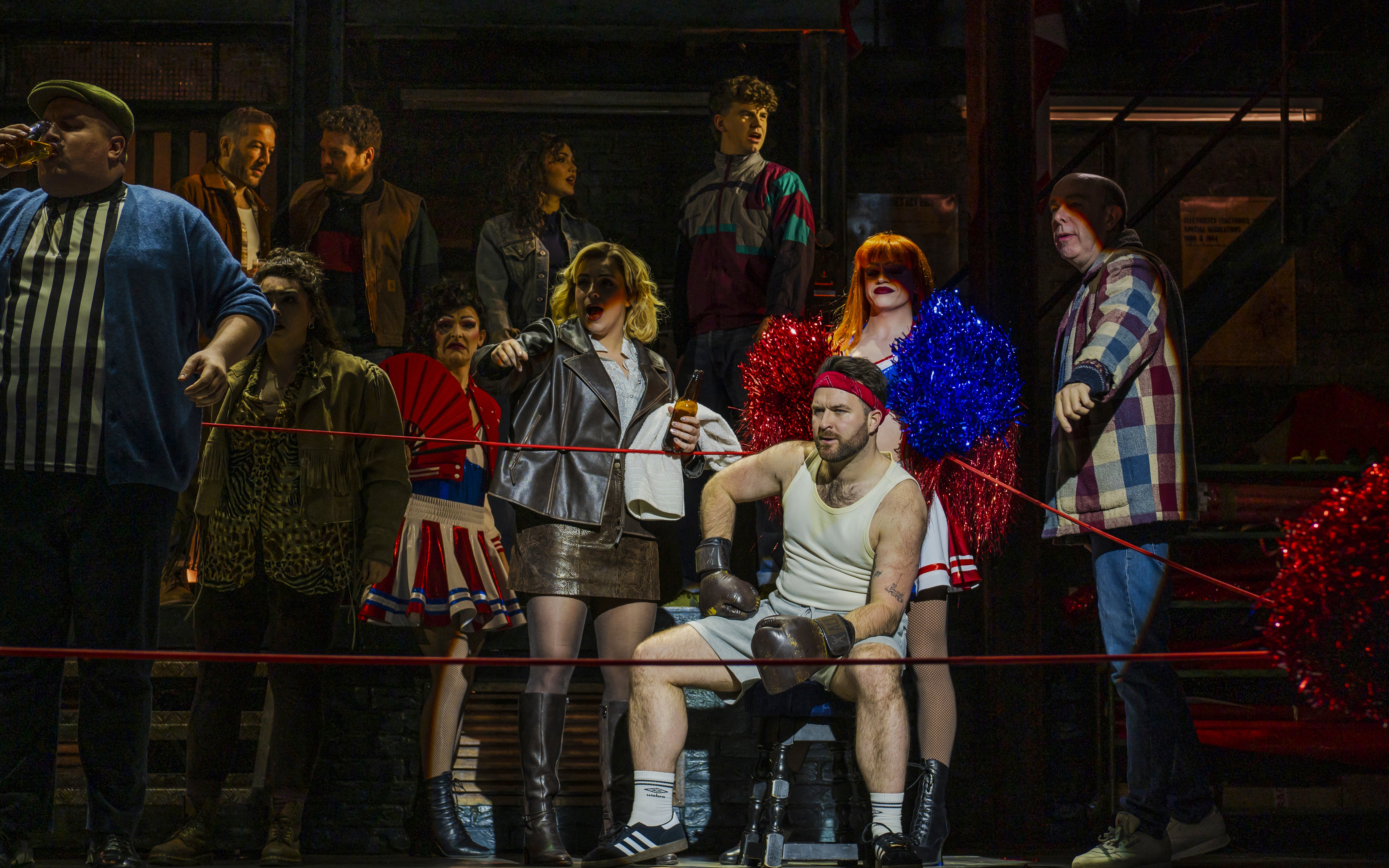 Cast performing a lively scene from Kinky Boots with a boxer in the foreground.