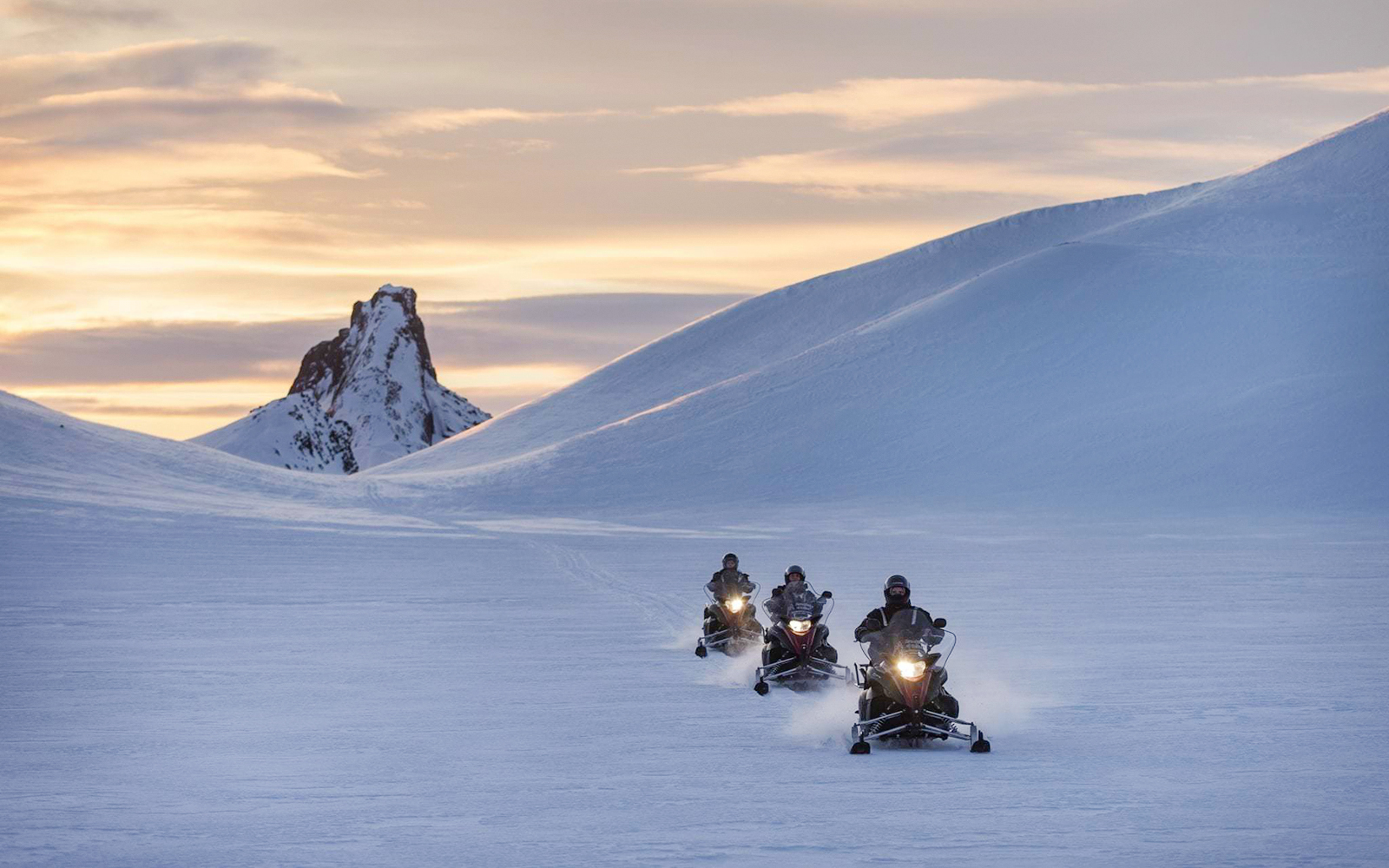 Snowmobilers riding on a glacier with a mountain backdrop during Secret Lagoon tour.