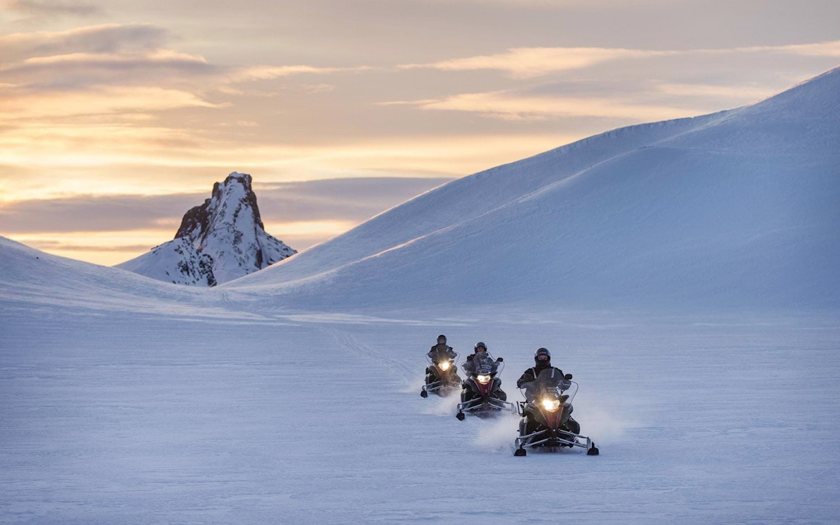 Snowmobilers riding on a glacier with a mountain backdrop during Secret Lagoon tour.