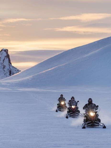 Snowmobilers riding on a glacier with a mountain backdrop during Secret Lagoon tour.
