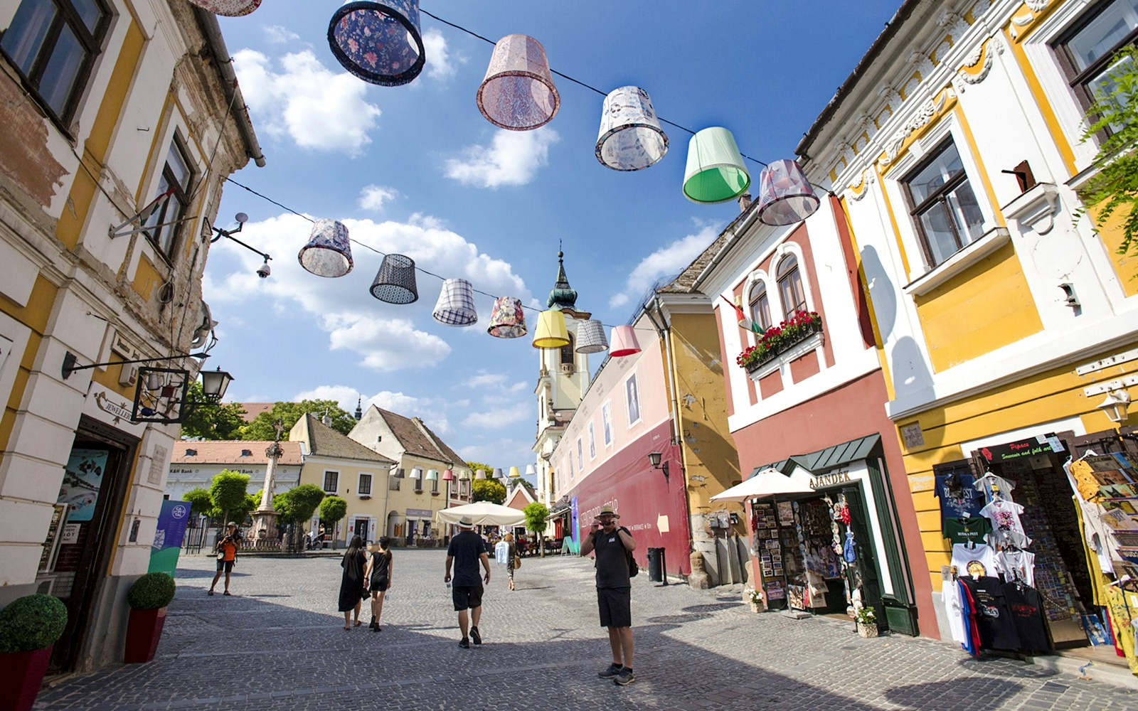 Guests walking through colorful streets of Szentendre, Hungary, with decorative hanging lamps.