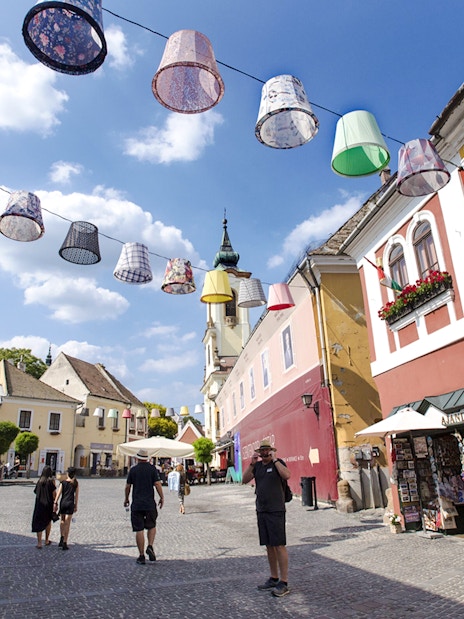 Guests walking through colorful streets of Szentendre, Hungary, with decorative hanging lamps.