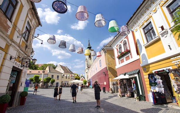 Guests walking through colorful streets of Szentendre, Hungary, with decorative hanging lamps.