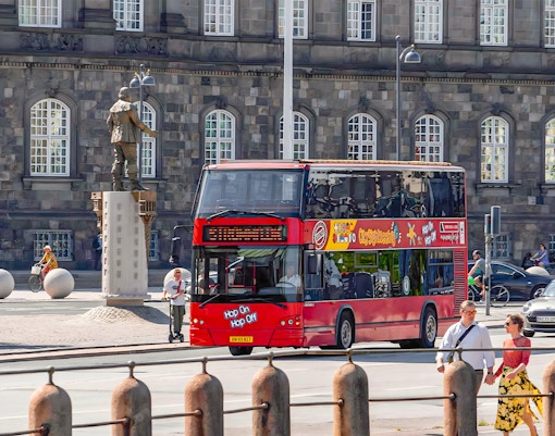 Copenhagen hop-on hop-off bus with tourists near colorful buildings.