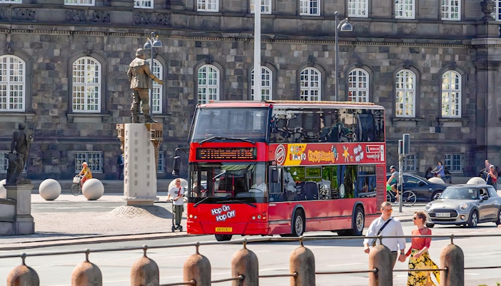 Copenhagen hop-on hop-off bus with tourists near Nyhavn canal and colorful buildings.