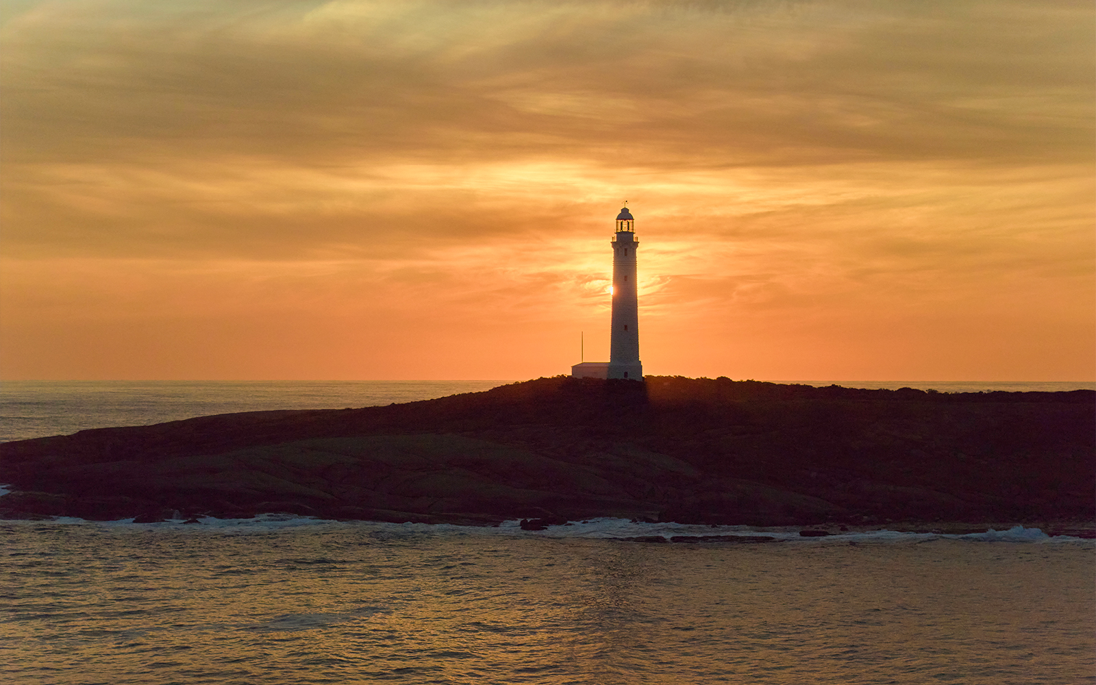 Cape Leeuwin Lighthouse silhouetted against sunset sky in Australia.