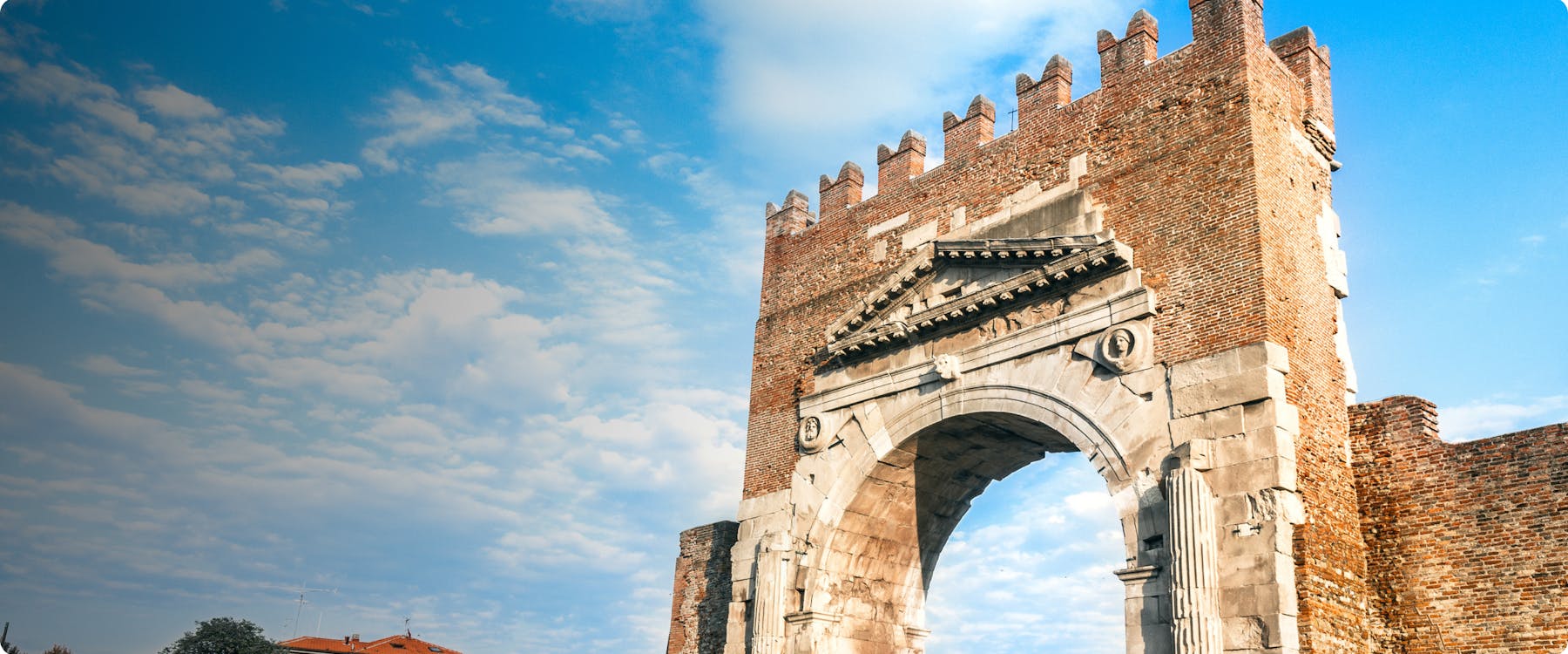 Ancient Roman arch in Rimini, Italy, under a blue sky.
