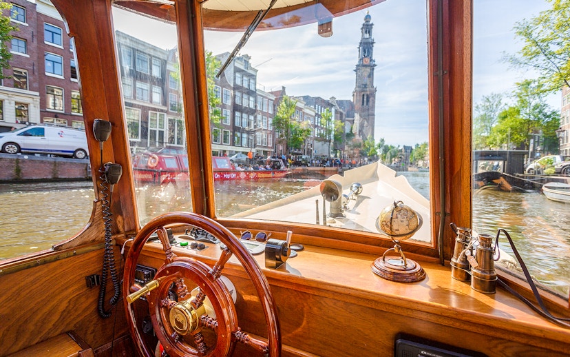Steering wheel and interior view from an Amsterdam canal cruise boat with Westerkerk in the background.