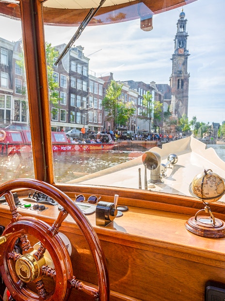 Steering wheel and interior view from an Amsterdam canal cruise boat with Westerkerk in the background.