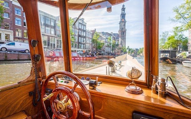 Steering wheel and interior view from an Amsterdam canal cruise boat with Westerkerk in the background.