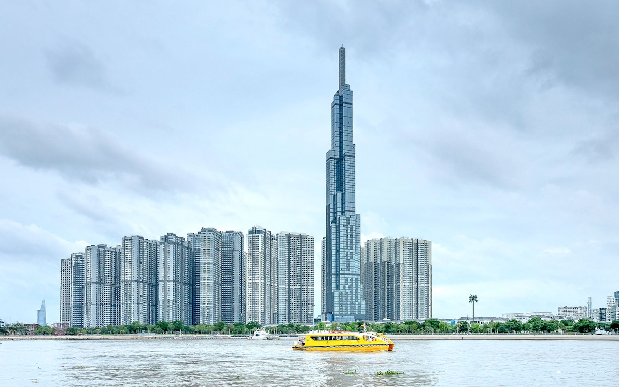 Landmark 81 and nearby skyscrapers by the river with a yellow ferry in Ho Chi Minh City.