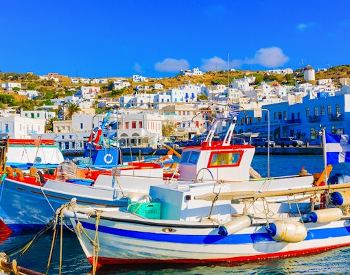 Fishing boats docked at the Old Port in Mykonos, Greece, with white buildings in the background.