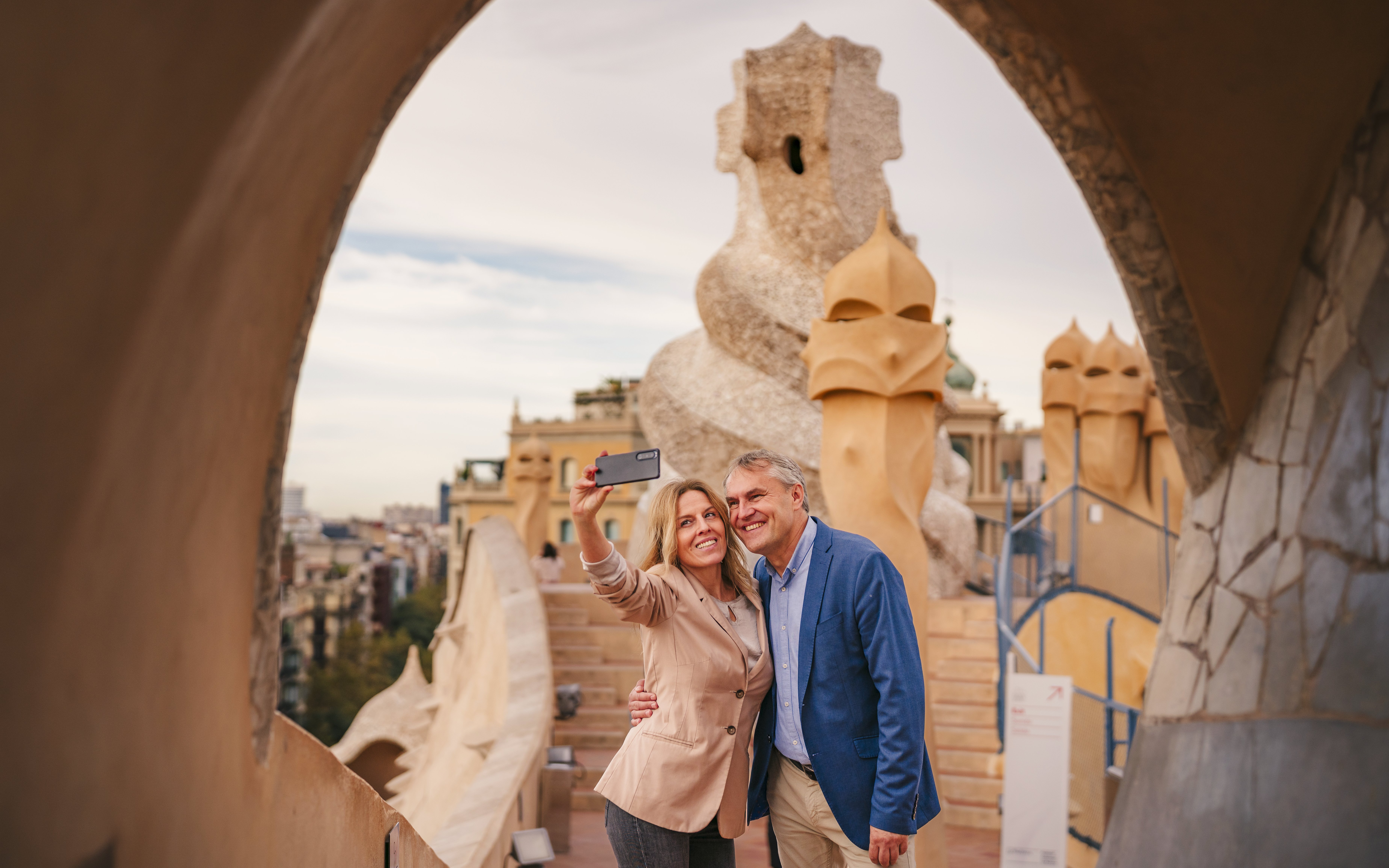 Tourists taking a selfie on the rooftop of Casa Mila, Barcelona, with unique chimney sculptures.
