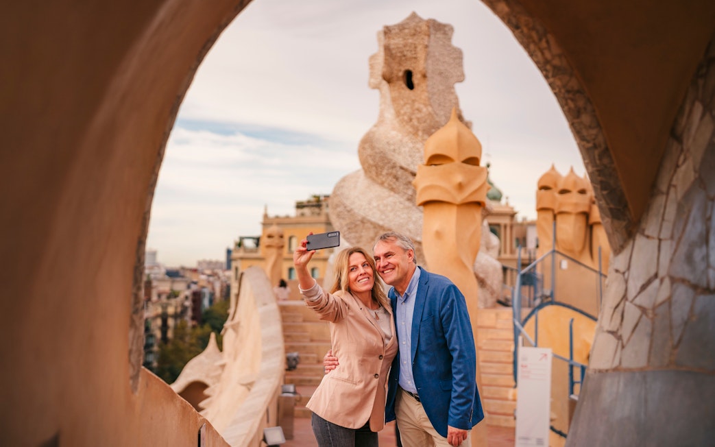 Tourists taking a selfie on the rooftop of Casa Mila, Barcelona, with unique chimney sculptures.