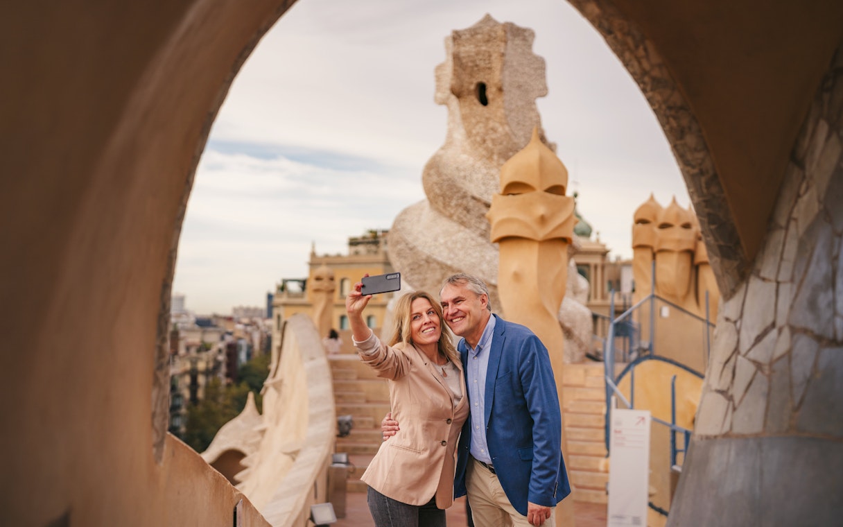 Tourists taking a selfie on the rooftop of Casa Mila, Barcelona, with unique chimney sculptures.