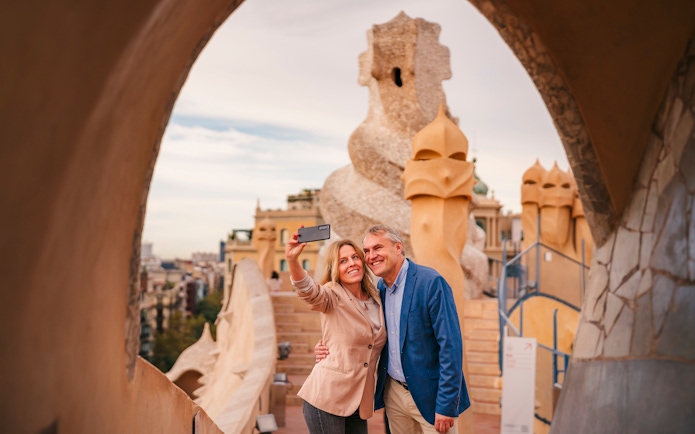 Tourists taking a selfie on the rooftop of Casa Mila, Barcelona, with unique chimney sculptures.
