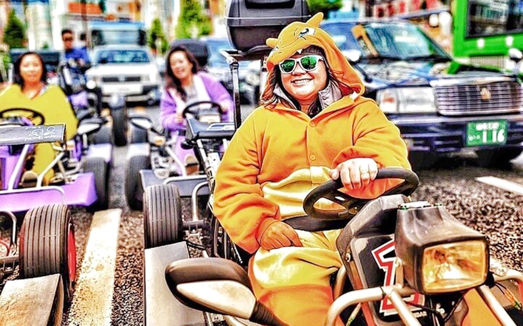 Person in Charmander costume driving a go-kart on a city street.