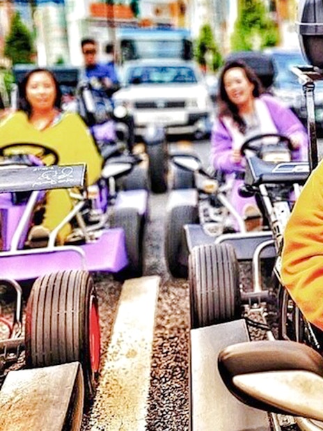 Person in Charmander costume driving a go-kart on a city street.
