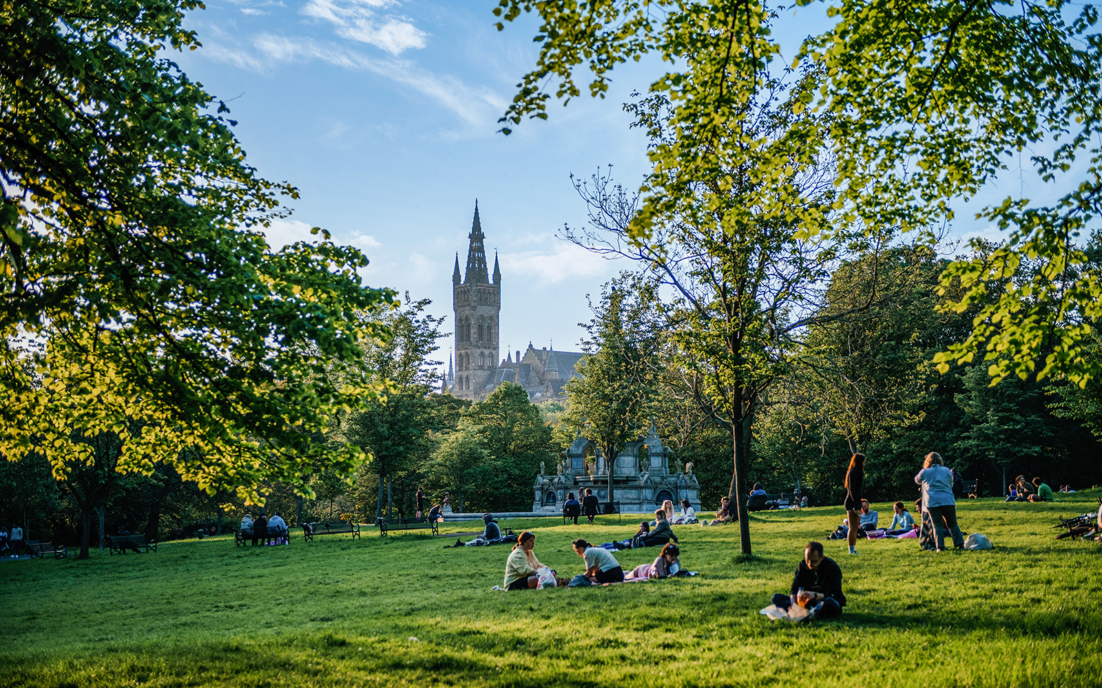 Visitors relaxing on the grass in Kelvingrove Park, Glasgow, with a view of the University tower.