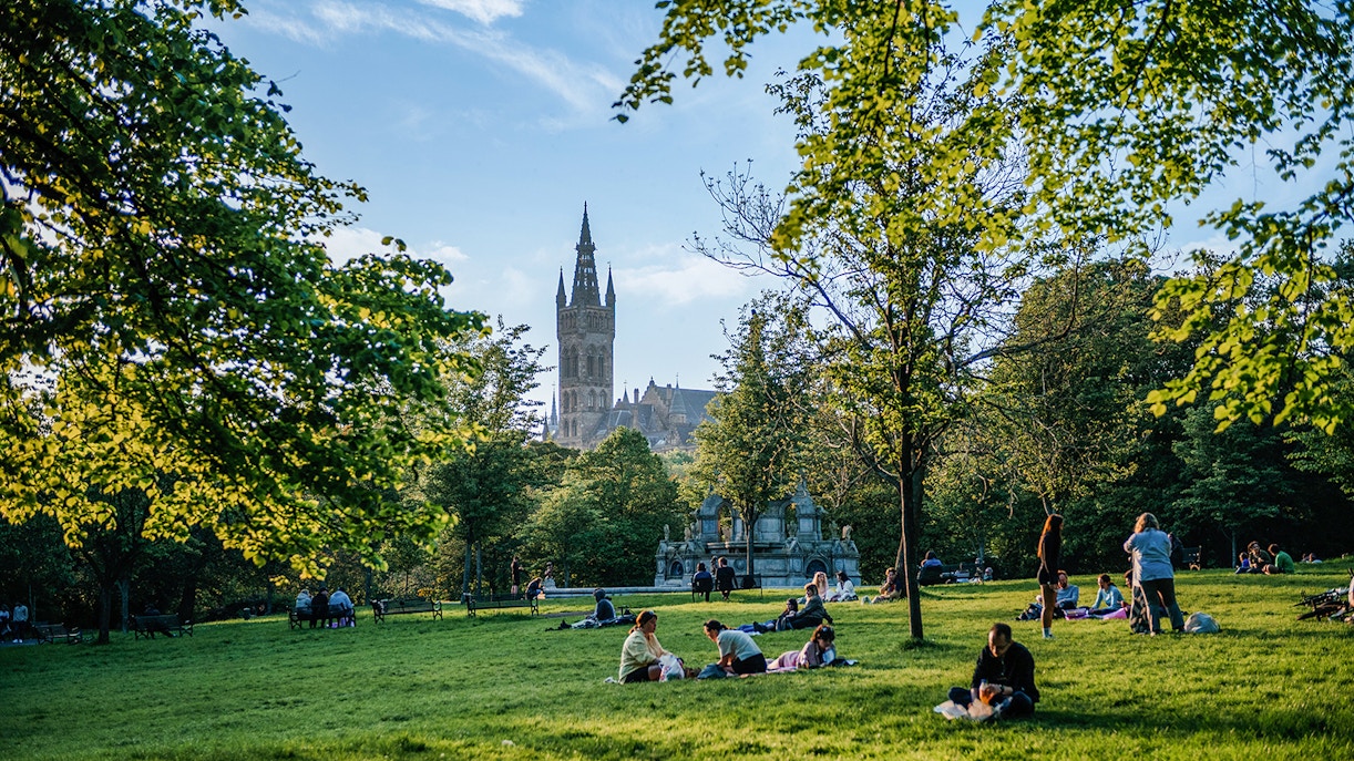 Visitors relaxing on the grass in Kelvingrove Park, Glasgow, with a view of the University tower.
