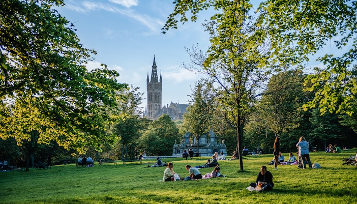 Visitors relaxing on the grass in Kelvingrove Park, Glasgow, with a view of the University tower.