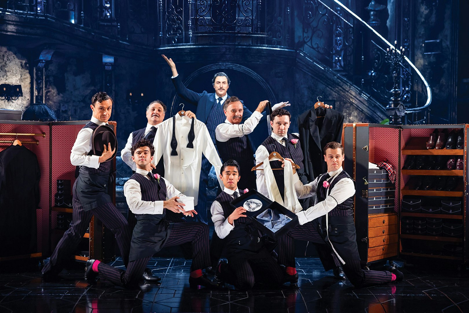Men in formal attire posing with suits and accessories on a theatrical stage, Sunset Boulevard.