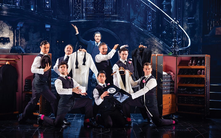 Men in formal attire posing with suits and accessories on a theatrical stage, Sunset Boulevard.