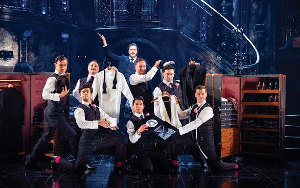 Men in formal attire posing with suits and accessories on a theatrical stage, Sunset Boulevard.