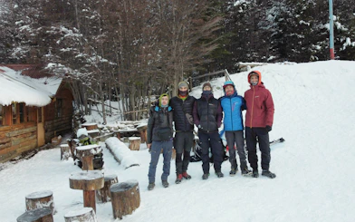Tourists standing on snow at Ushuaia Martial Glacier with wooden cabin and trees in background.