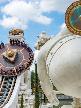 Visitors on a spinning ride at Parc Astérix, Paris, with a large statue in the foreground.