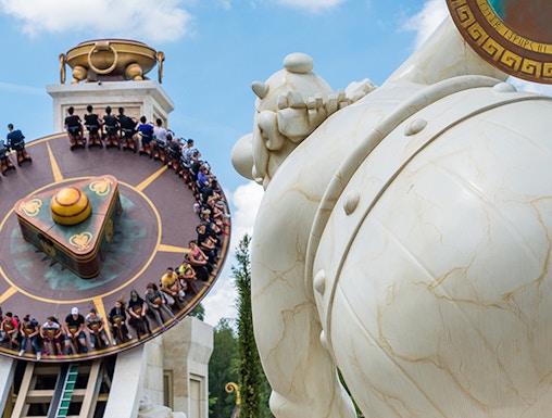 Visitors on a spinning ride at Parc Astérix, Paris, with a large statue in the foreground.
