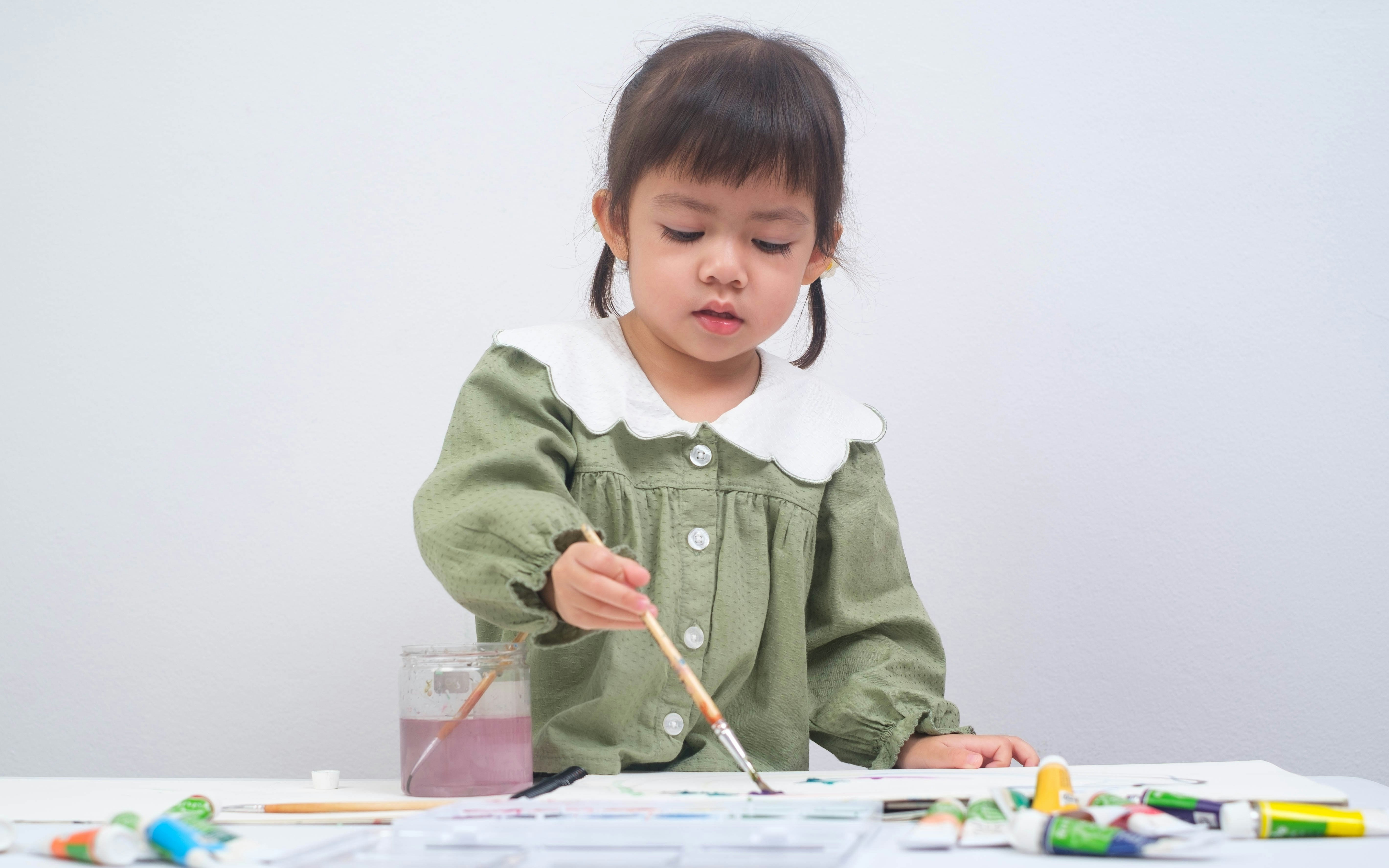 Girl painting on white canvas with brushes and paints.