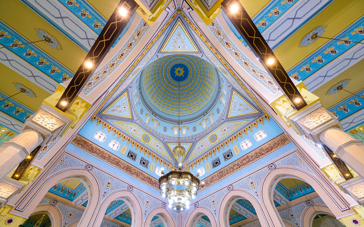 Intricate ceiling of a mosque in Dubai with colorful geometric patterns and a central chandelier.