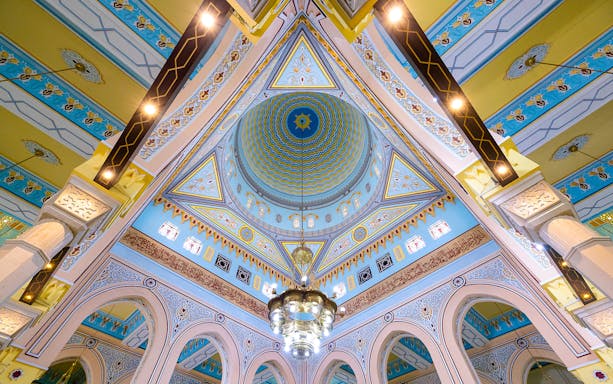 Intricate ceiling of a mosque in Dubai with colorful geometric patterns and a central chandelier.