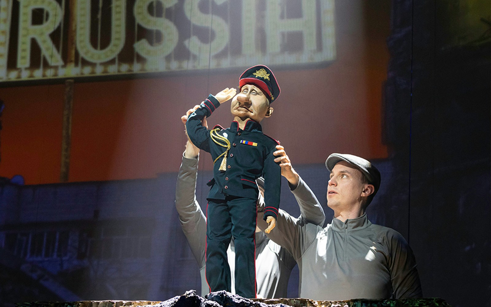 Puppeteer controlling a military puppet in "Idiots Assemble: Spitting Image the Musical" scene.