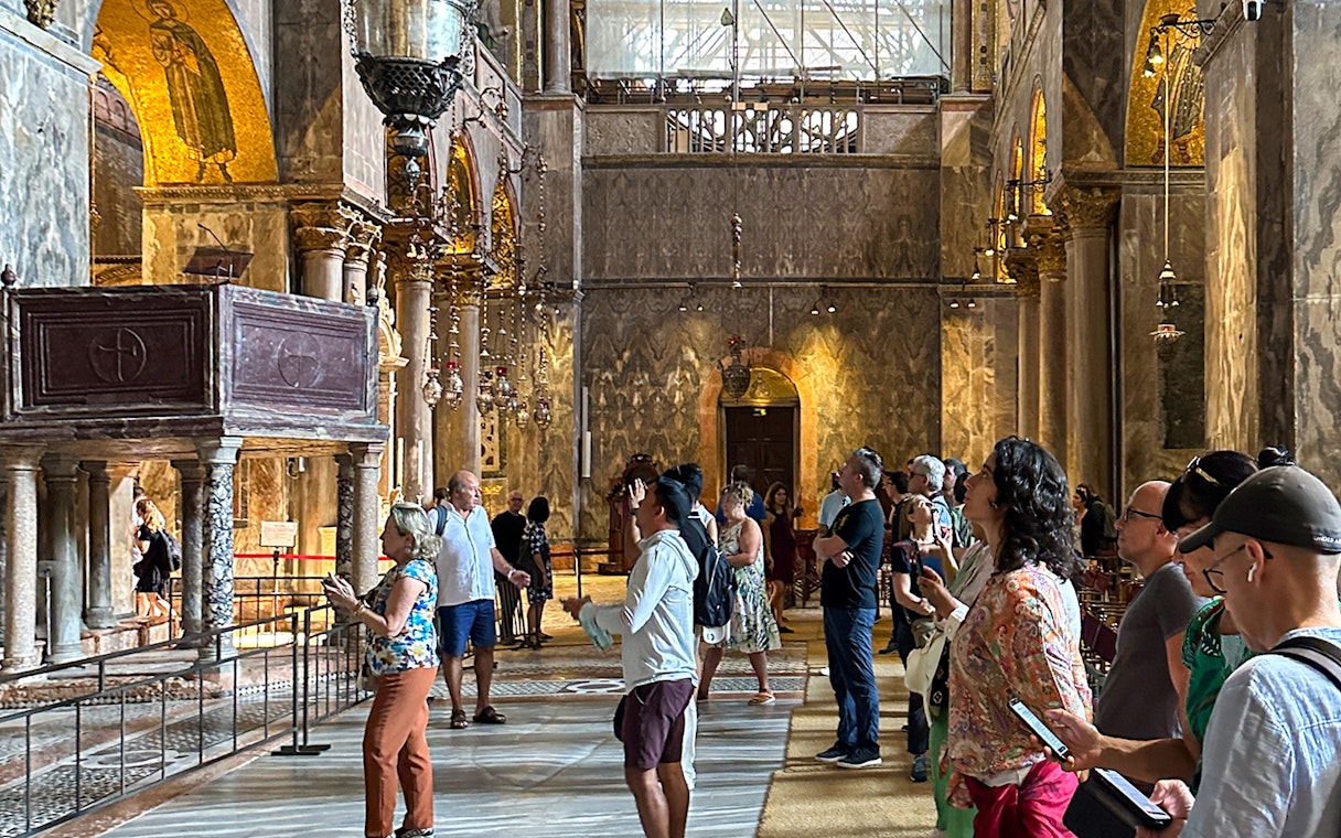 Visitors inside St. Mark's Basilica, Venice, using audioguides to explore the ornate interior.