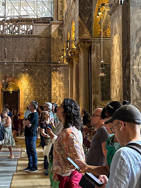 Visitors inside St. Mark's Basilica, Venice, using audioguides to explore the ornate interior.